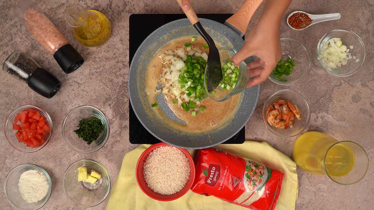 L'ajout d'oignons et de poivrons verts dans le roux brun, étape clé de la préparation de l'étouffée de crevettes, avec les autres ingrédients disposés autour.