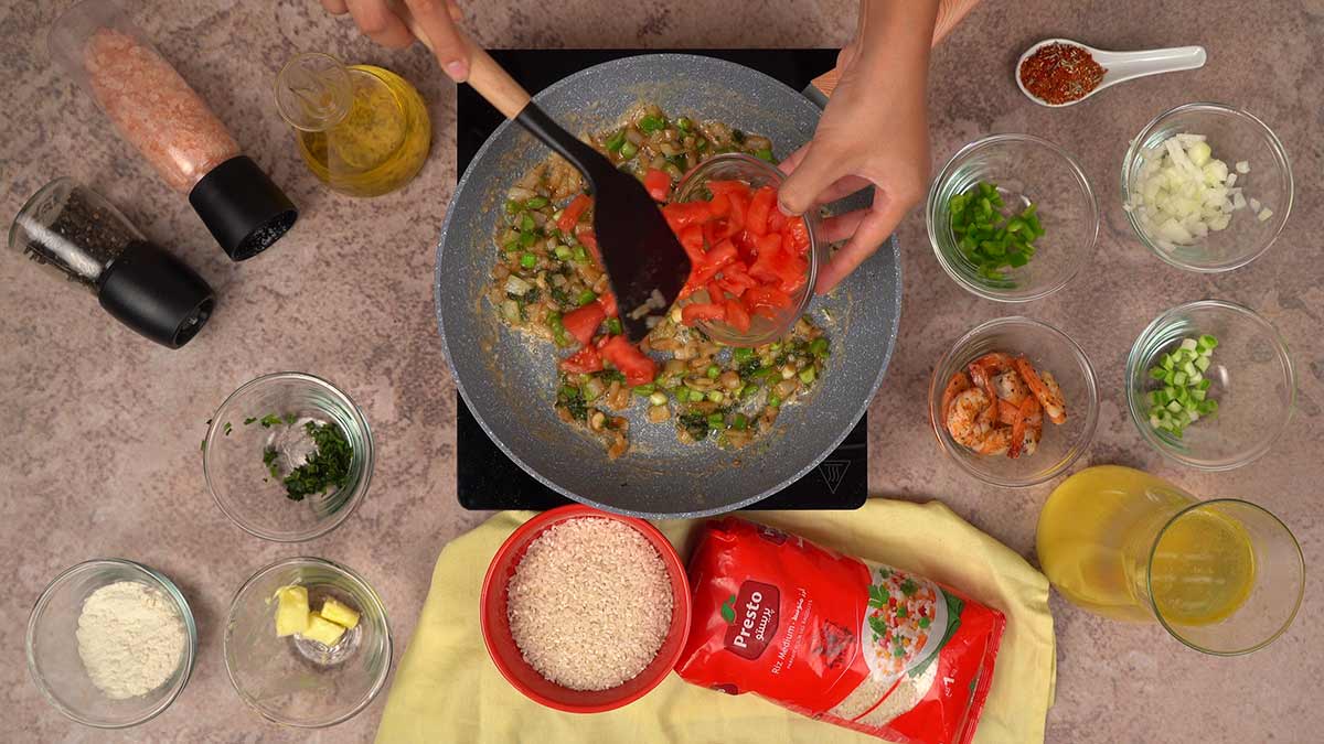 L'ajout de tomates fraîches coupées en dés dans la poêle contenant le mélange d'oignons, de poivrons et d'autres légumes déjà sautés.