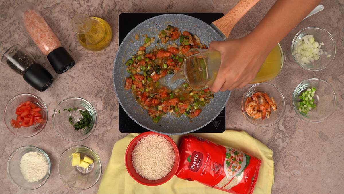 L'ajout de bouillon au mélange de légumes sautés, notamment des tomates, poivrons et oignons.