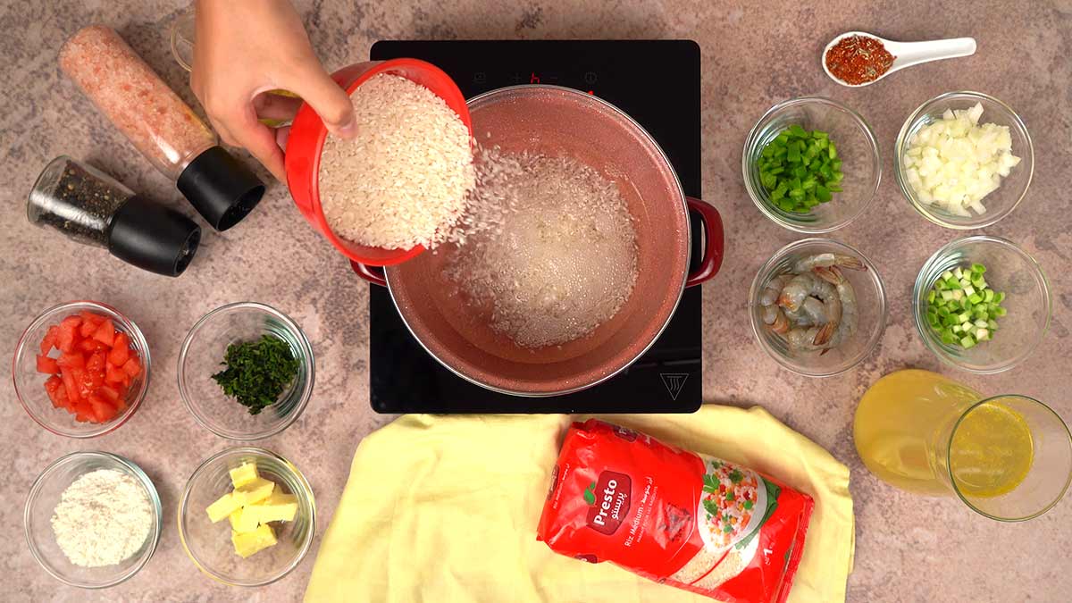 La préparation de l'etoufee avec des ingrédients frais comme le riz médium Presto, légumes, crevettes et épices, disposés autour d'une casserole sur une plaque de cuisson.