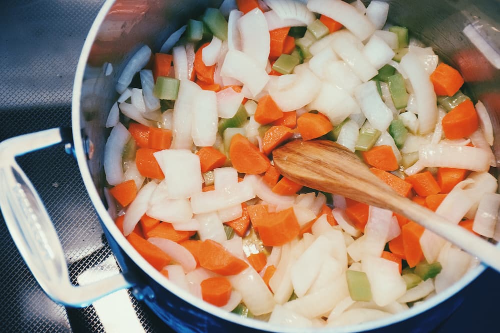 Des carottes, du céleri et des oignons mijotent dans une marmite, diffusant leurs arômes parfumés formant une base de cuisine pour une soupe