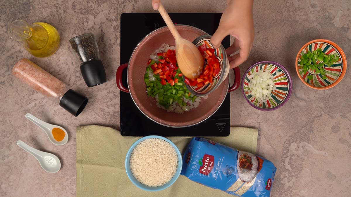 L'ajout de poivrons rouges et verts dans une casserole contenant des oignons sautés.