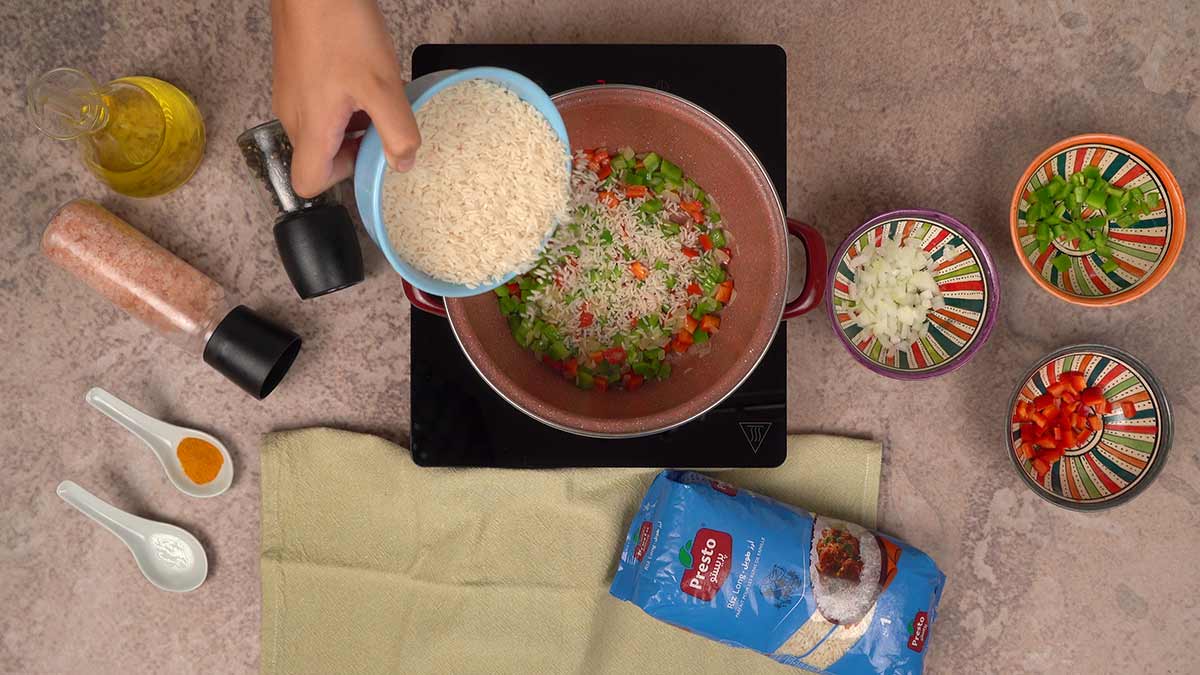 L'ajout de riz long Presto dans la casserole contenant un mélange de poivrons rouges, poivrons verts et oignons sautés.