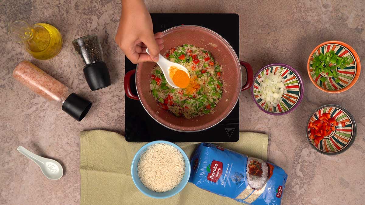 L'ajout de curry au casserole contenant un mélange de riz, poivrons rouges et verts, et oignons.