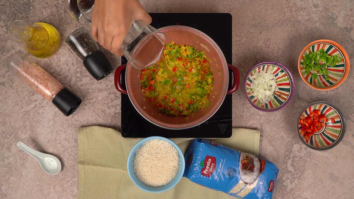 L'ajout d'eau dans une casserole contenant le mélange de riz Presto, poivrons, oignons et curry.