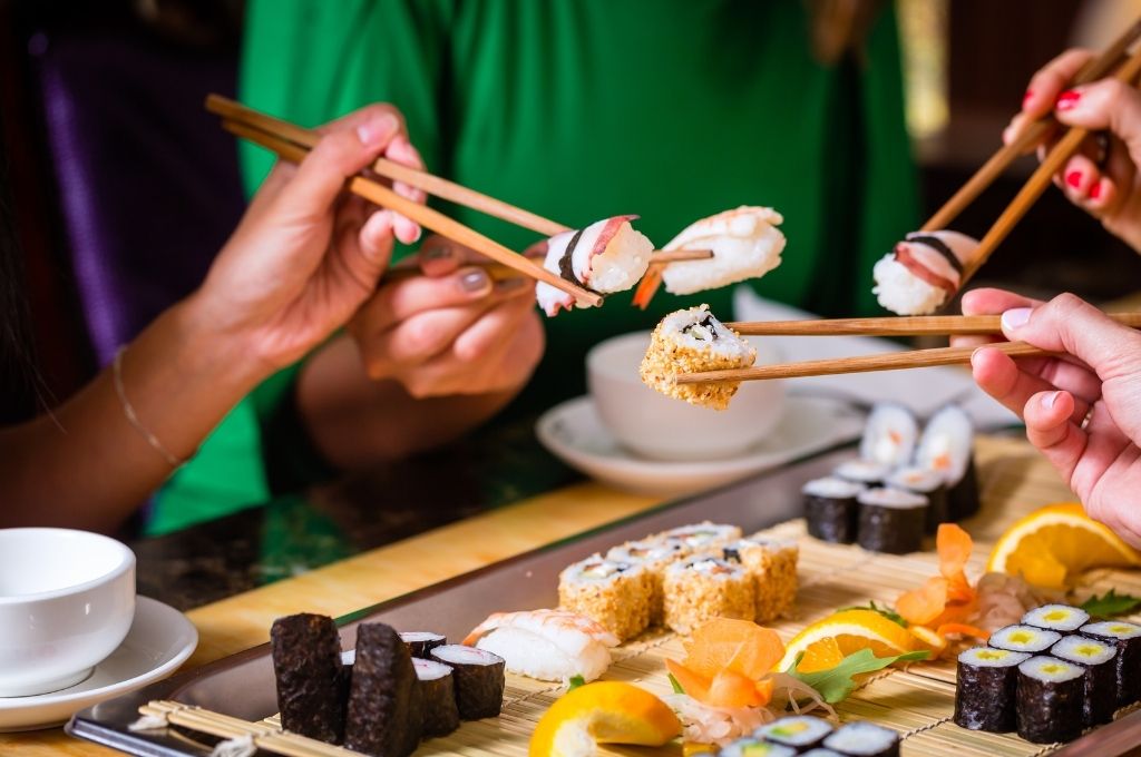 Un groupe de personnes partageant un plateau varié de sushis et makis, utilisant des baguettes pour savourer les différentes pièces, dans une ambiance conviviale et chaleureuse.