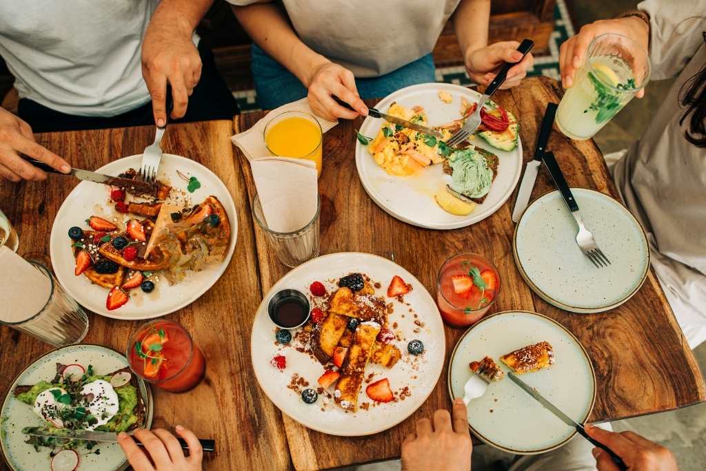 Vue d'en haut de plusieurs personnes partageant un brunch avec des gaufres et des toasts sur une table en bois.