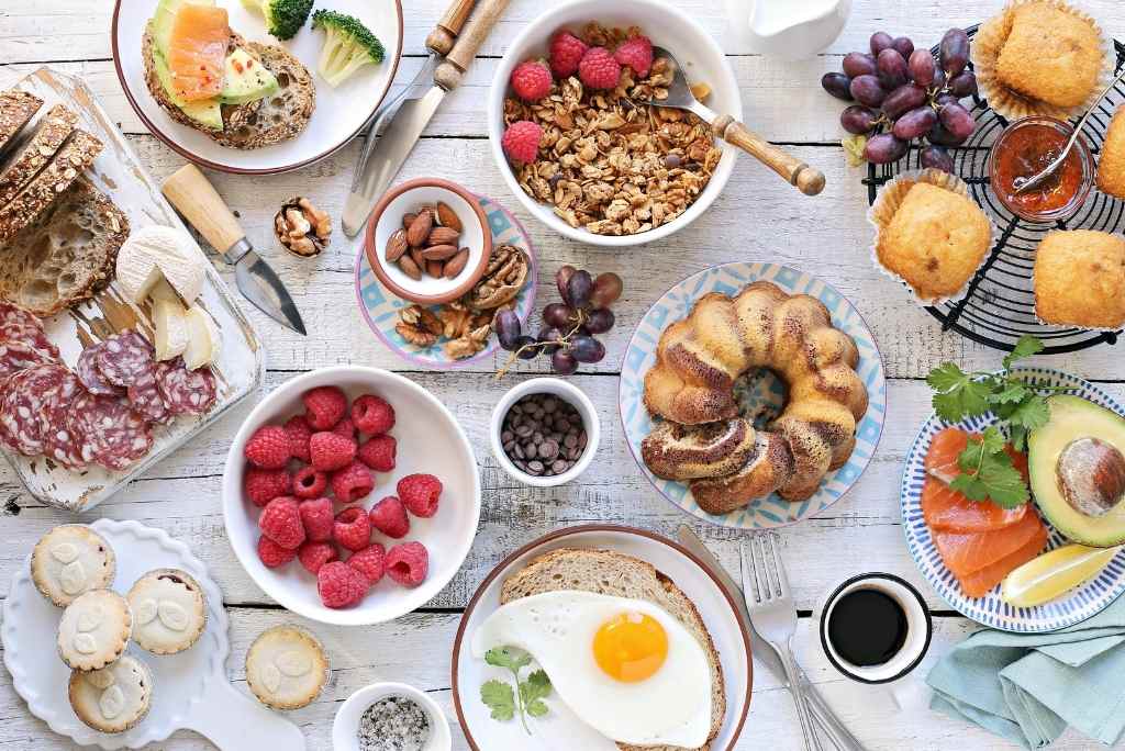 Vue d'en haut d'une table en bois rustique garnie d'un brunch copieux et coloré, avec un œuf au plat, des plats salés, des pâtisseries et des fruits frais.