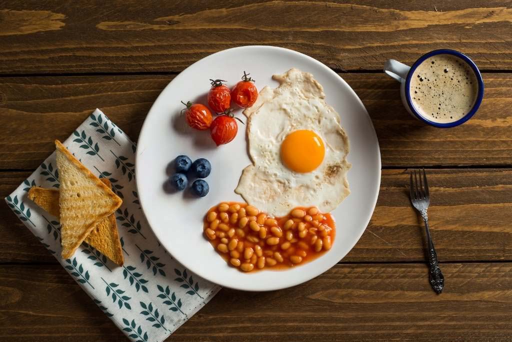 Un petit-déjeuner composé d'un œuf au plat, de haricots, de tomates et de toasts, vu d'en haut sur une table en bois.
