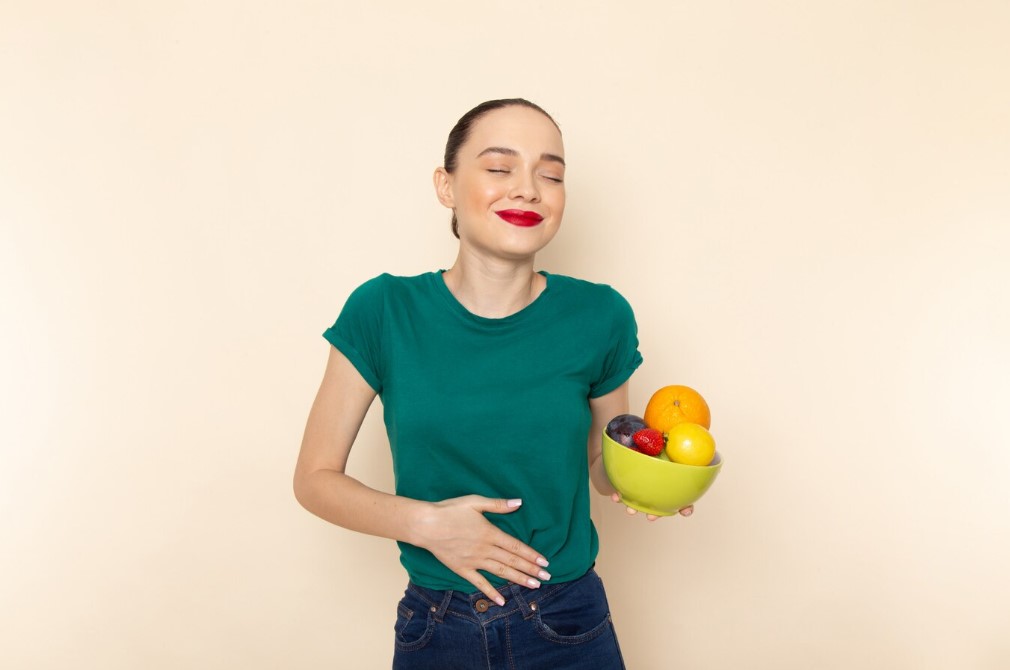 une dame qui est satisfaite de sa digestion et portant un bol de fruits variés