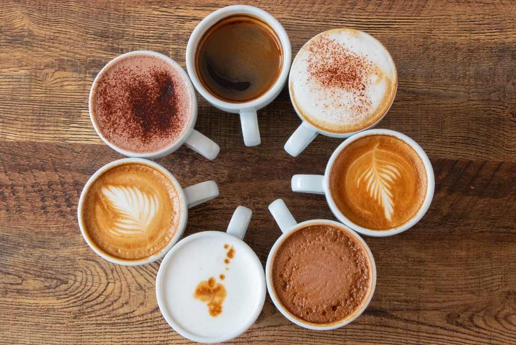 Un arrangement circulaire de sept tasses de café et de chocolat chaud sur une table en bois.