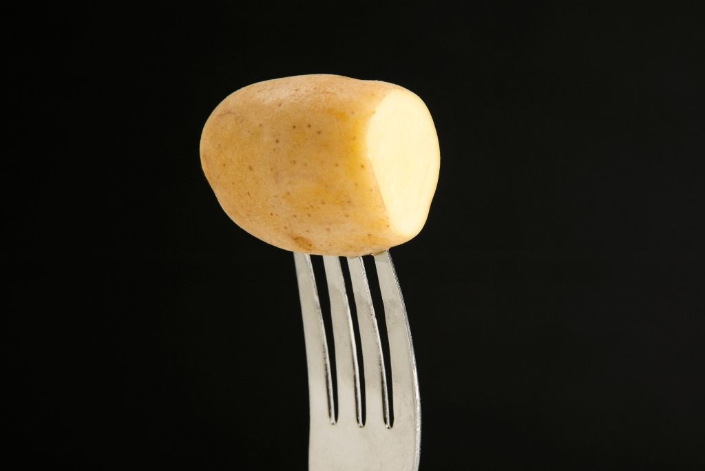 تحكّموا في نضج طعامكم شوكة مغروسة في قطعة بطاطس على خلفية سوداء.