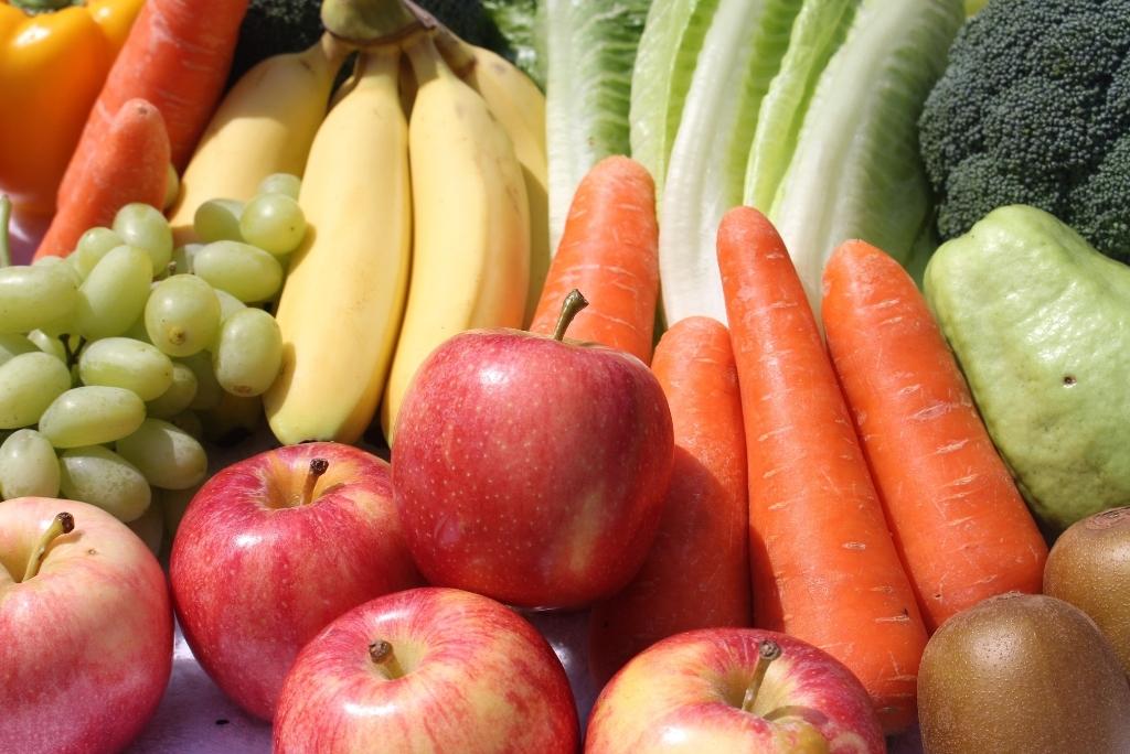 Gros plan sur un assortiment frais et varié de légumes et fruits : pommes rouges, carottes, bananes, raisins verts, brocoli et kiwis.