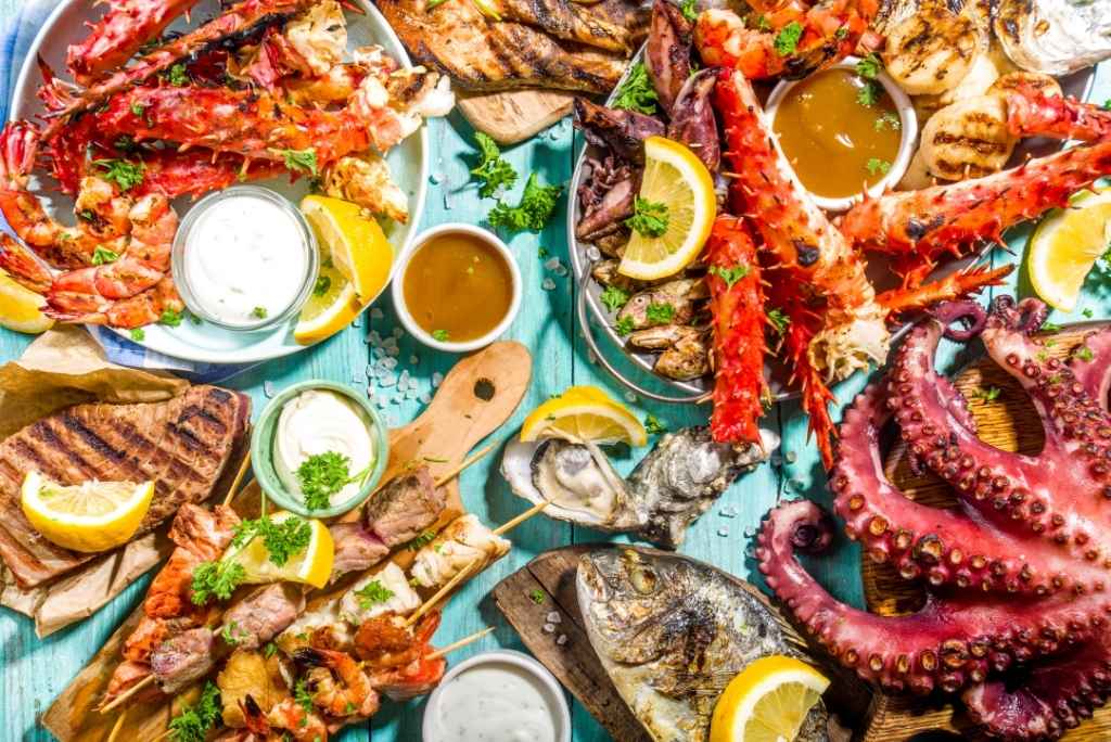 Assortiment coloré de poissons et fruits de mer grillés : homard, crabe, poulpe, huîtres et brochettes, accompagnés de sauces et de citrons