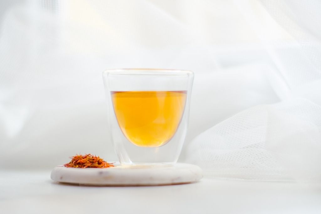 نقع الزعفران في كوب زجاجي مزدوج الجدار، يُظهر مشروباً ذهبياً صحياً مع خيوط الزعفران بجانبه.