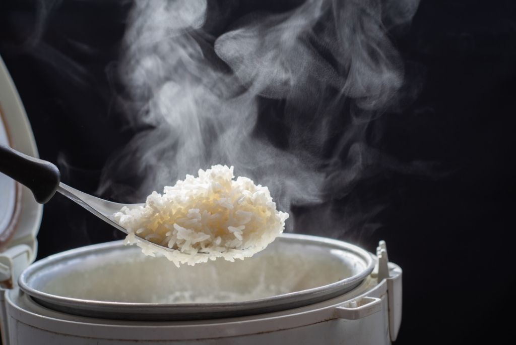 Gros plan d'une louche sortant du riz blanc fraîchement cuit et fumant d'un autocuiseur, illustrant des techniques de cuisson efficaces pour des repas sains