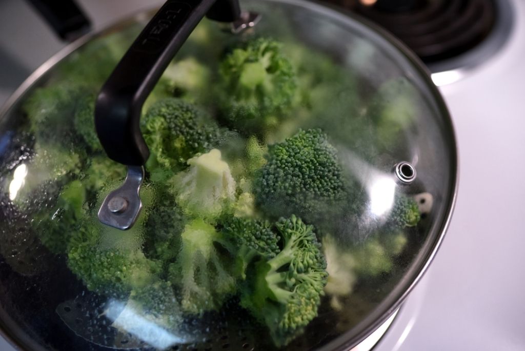 اكتشفوا خيارات ذكية للطهي بالبخار قدر يحتوي على مصفاة مدمجة مليئة بالبروكلي أثناء الطهي بالبخار، مع غطاء زجاجي شفاف.