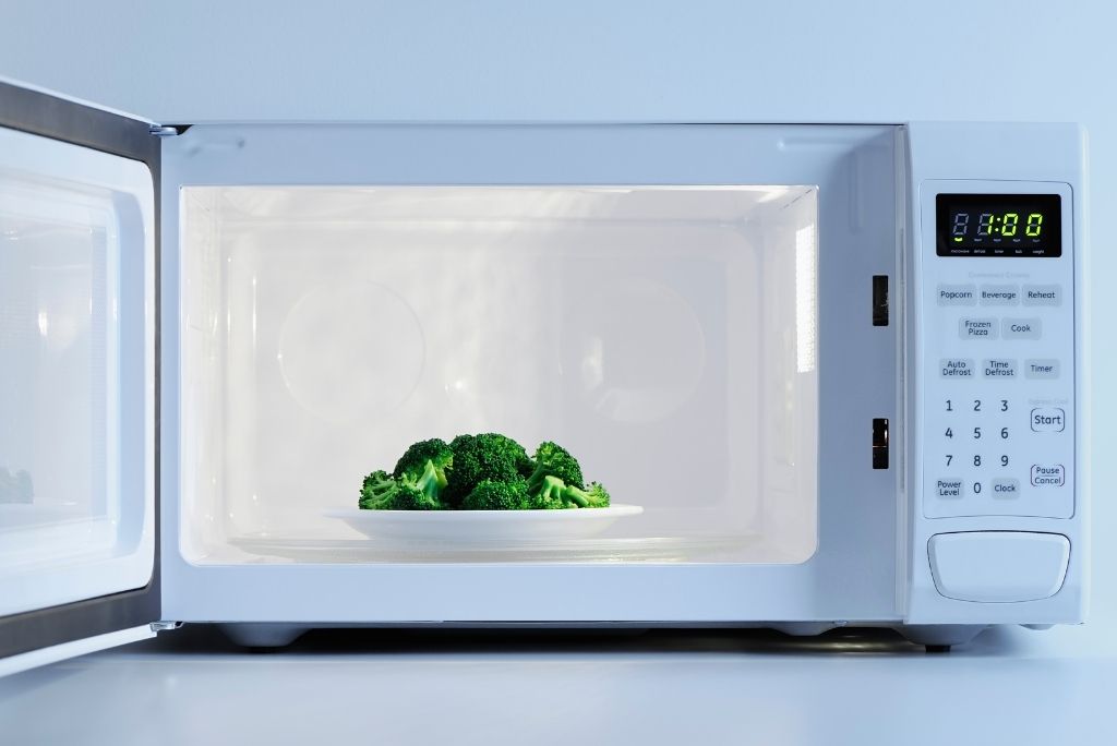 Tirez parti de cet appareil polyvalent Brocoli frais dans un four à micro-ondes blanc ouvert, prêt à être chauffé ou cuit.
