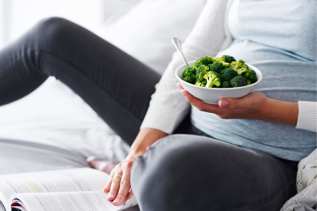 Personne enceinte avec des bols de brocoli, un des aliments riches en acide folique cruciaux durant la grossesse.