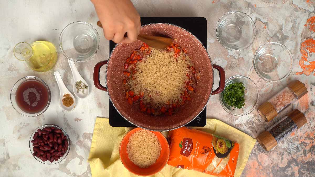 Une personne verse un bol de riz étuvé Presto dans la casserole avec les légumes et les épices. 