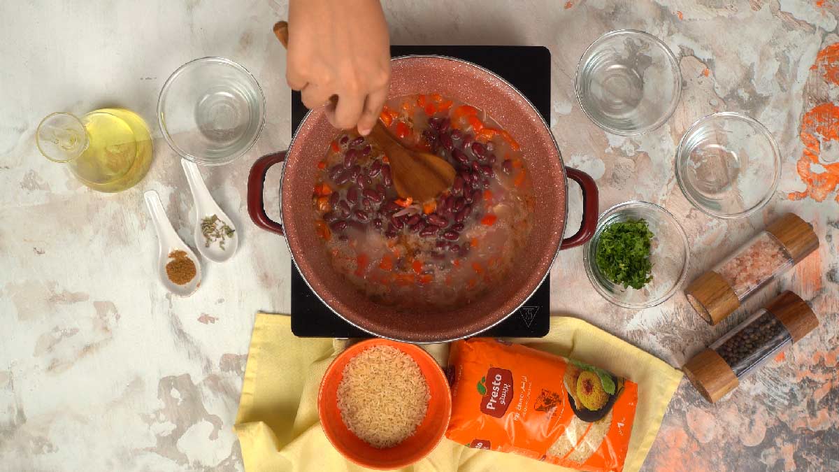 Une personne ajoute et mélange des haricots rouges cuits avec le riz et les légumes dans la casserole. 