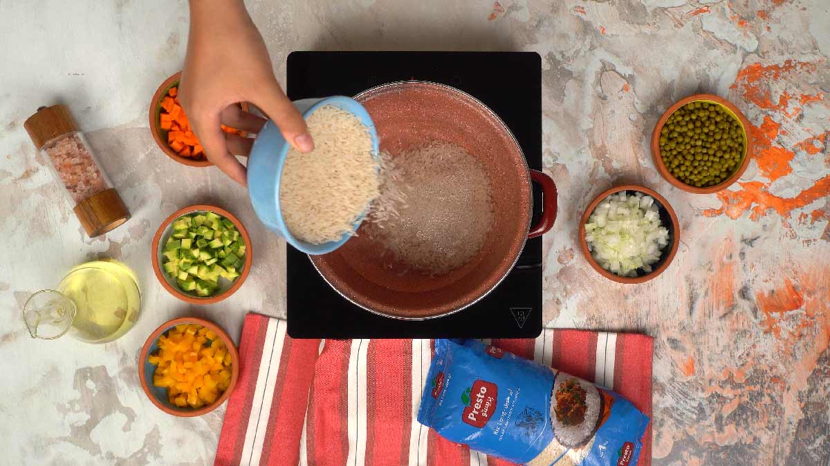 شخص يسكب أرز بريستو من وعاء أزرق في قدر لطهيه.
