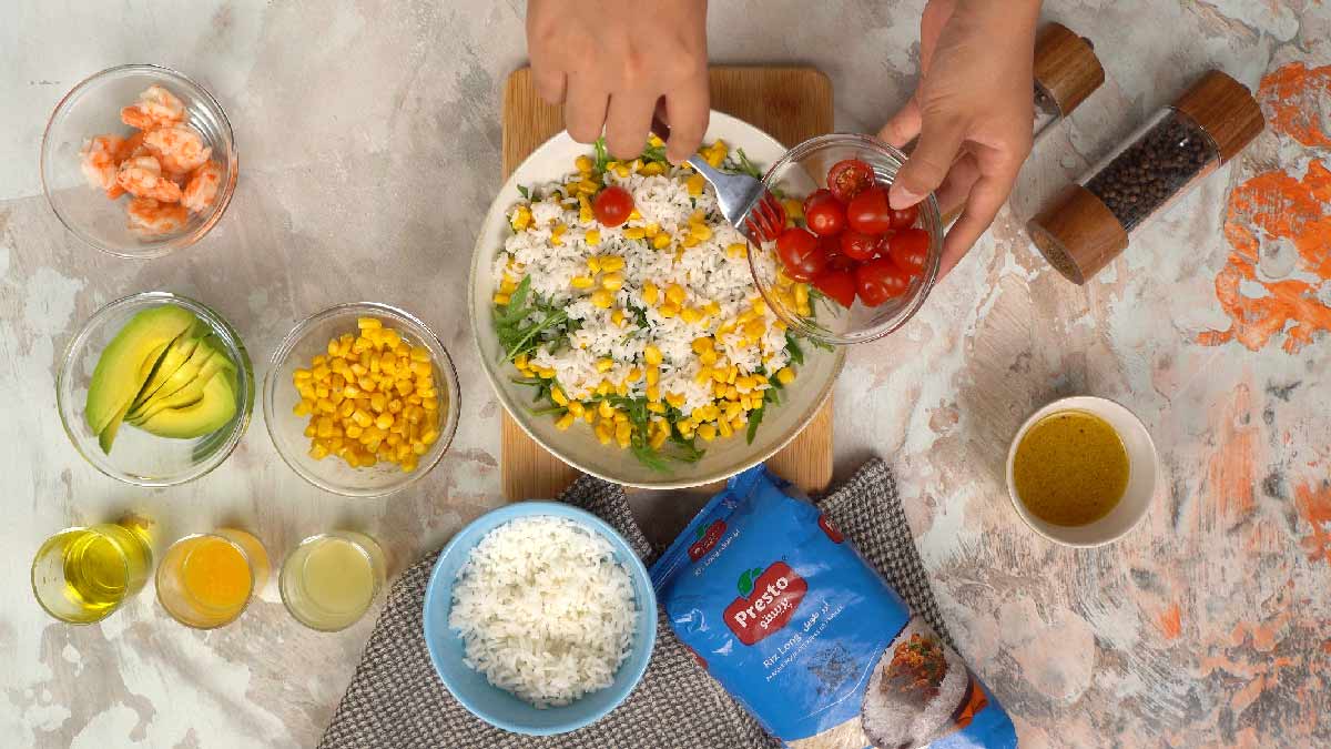 أيدٍ تضيف الطماطم الكرزية إلى الطبق الذي يحتوي بالفعل على الأرز والجرجير والذرة.
