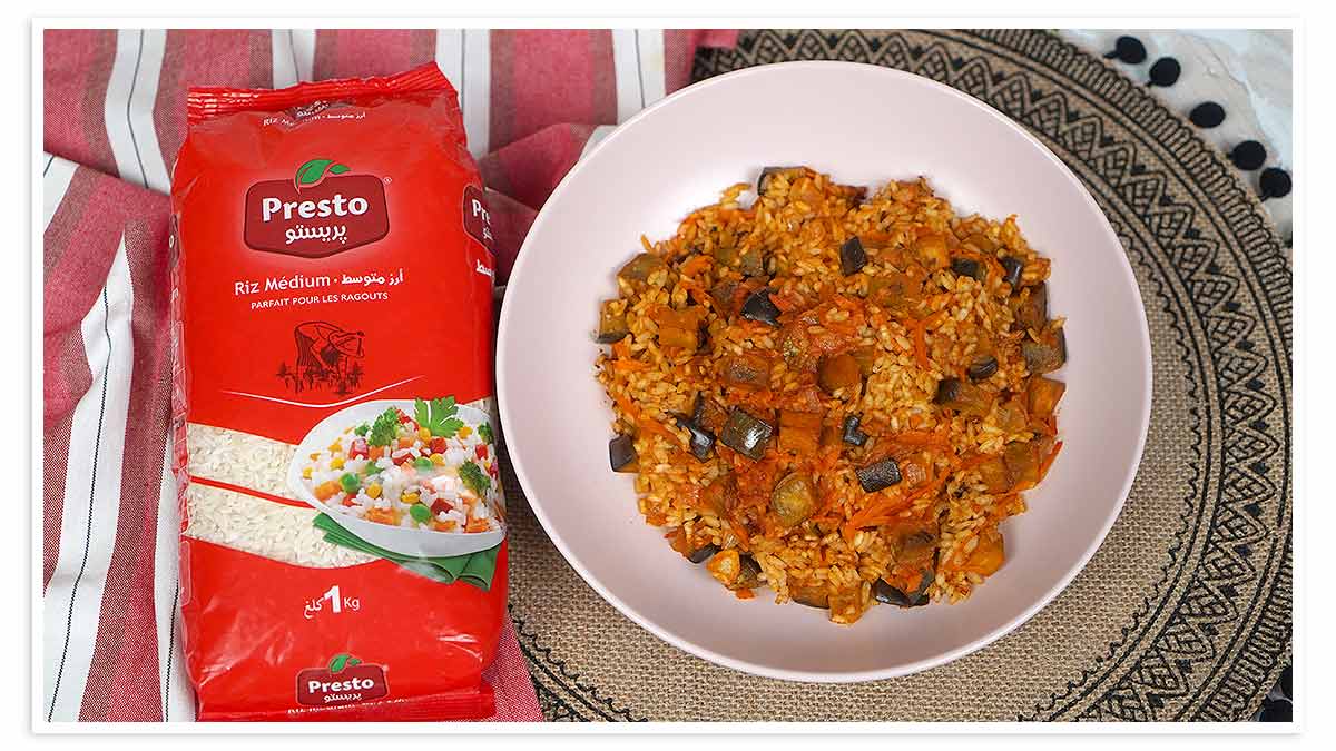 Un plat de riz aux aubergines, avec des carottes et d'autres légumes, est servi dans une assiette rose.