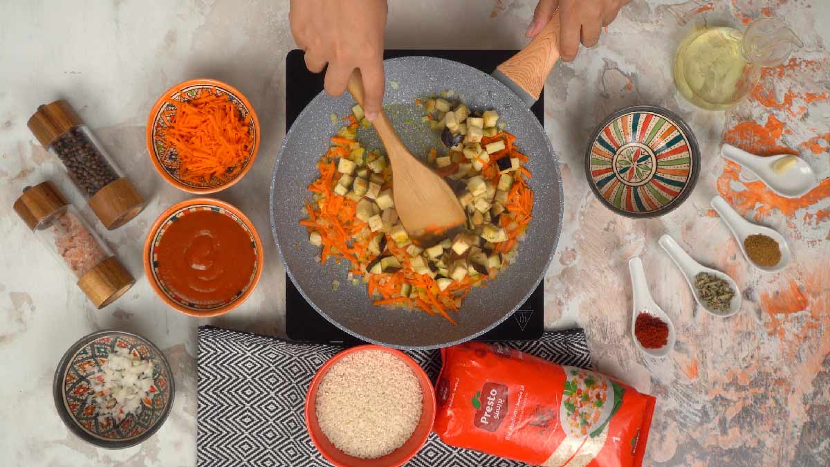 Des dés d'aubergine sont ajoutés dans la poêle et mélangés avec les carottes et les oignons. 