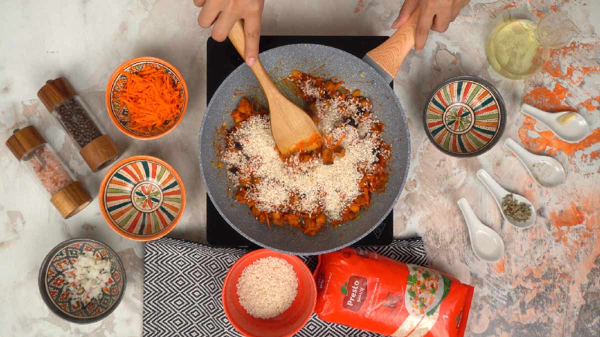 Une personne verse du riz moyen Presto dans la poêle pour le faire cuire avec les légumes et la sauce. 