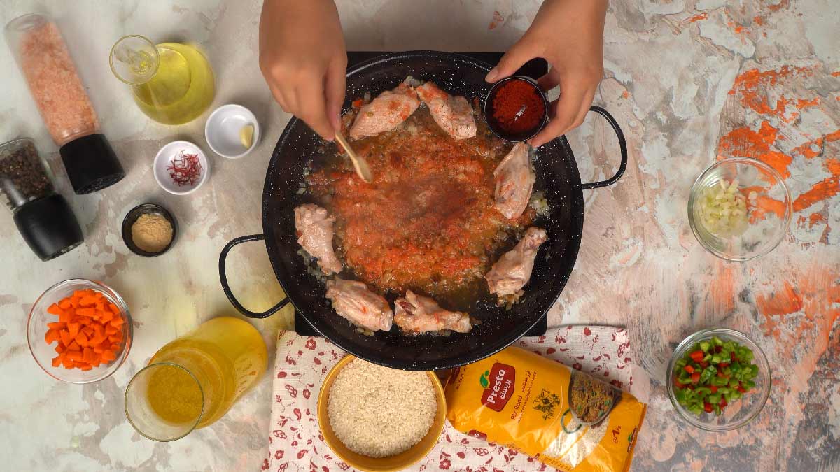 Une personne verse du paprika, sur les morceaux de poulet et les oignons dans la poêle.