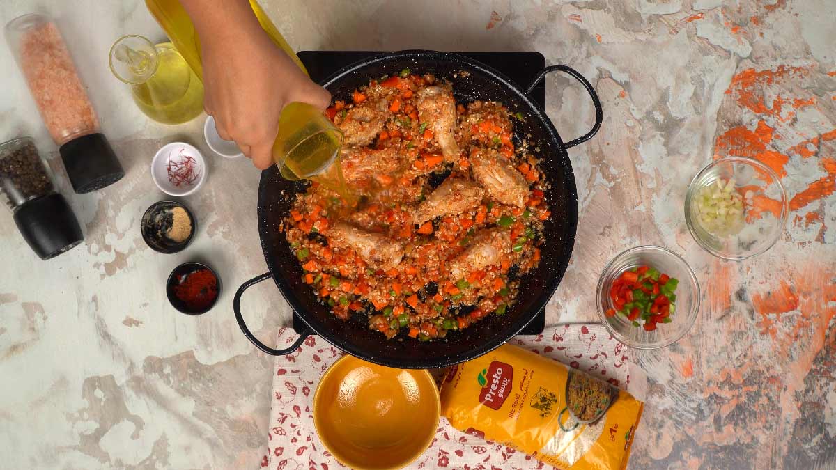 Une personne verse un bouillon d'un verre dans la poêle pour la cuisson du riz.
