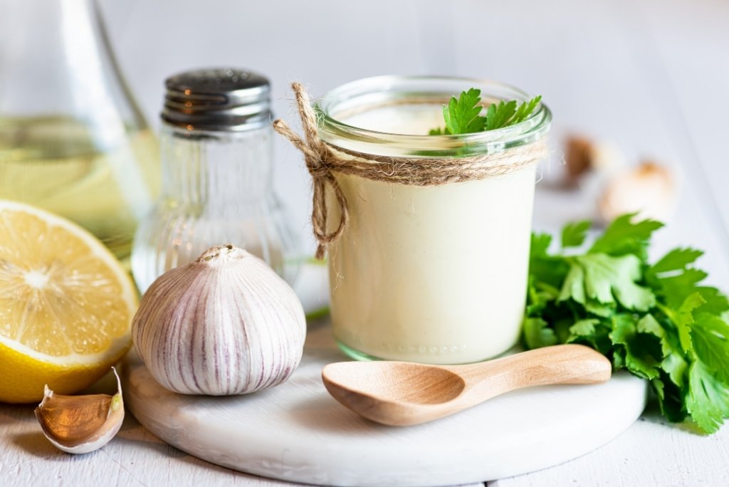وعاء صلصة أيولي بالثوم الكريمي، مع الليمون والبقدونس كمكونات.