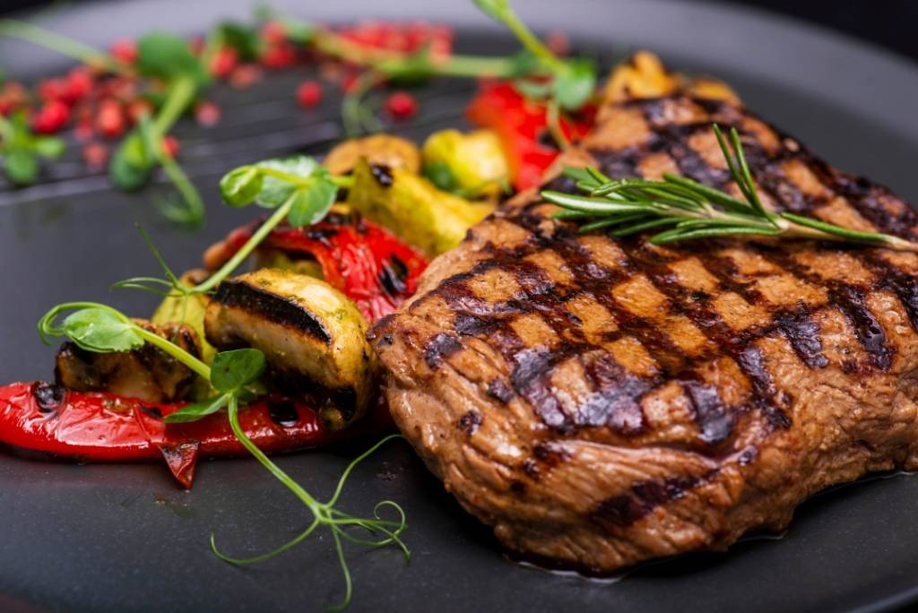 قطعة جميلة من اللحم المشوي تقدم مع الخضار المشوية على طبق داكن.