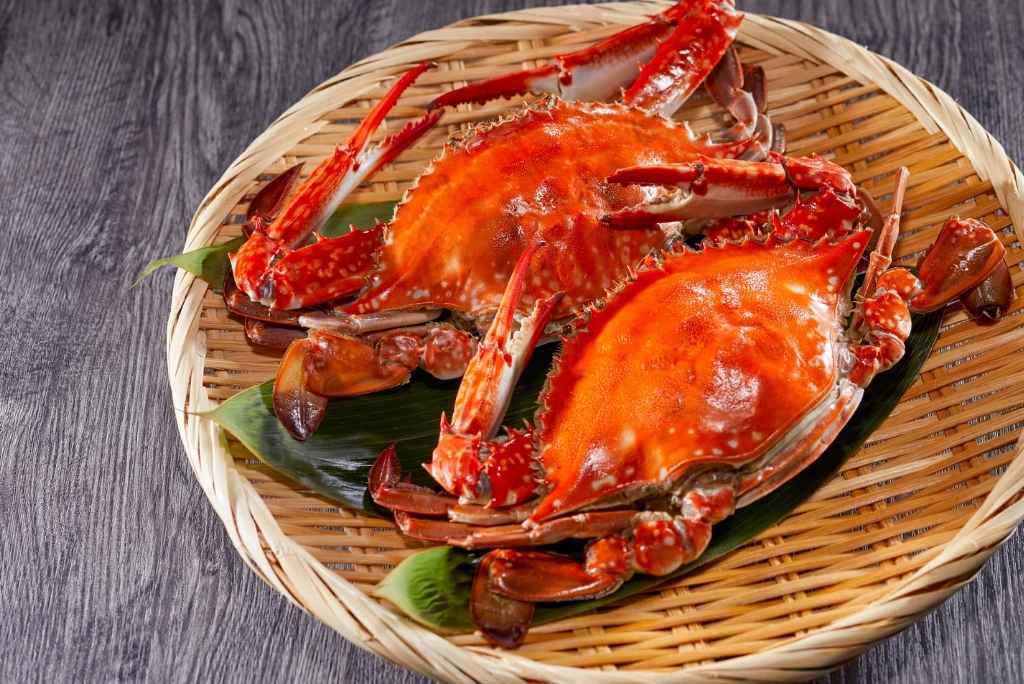 سرطانان بحريان مطهيان باللون الأحمر البرتقالي موضوعان على طبق من الخيزران.