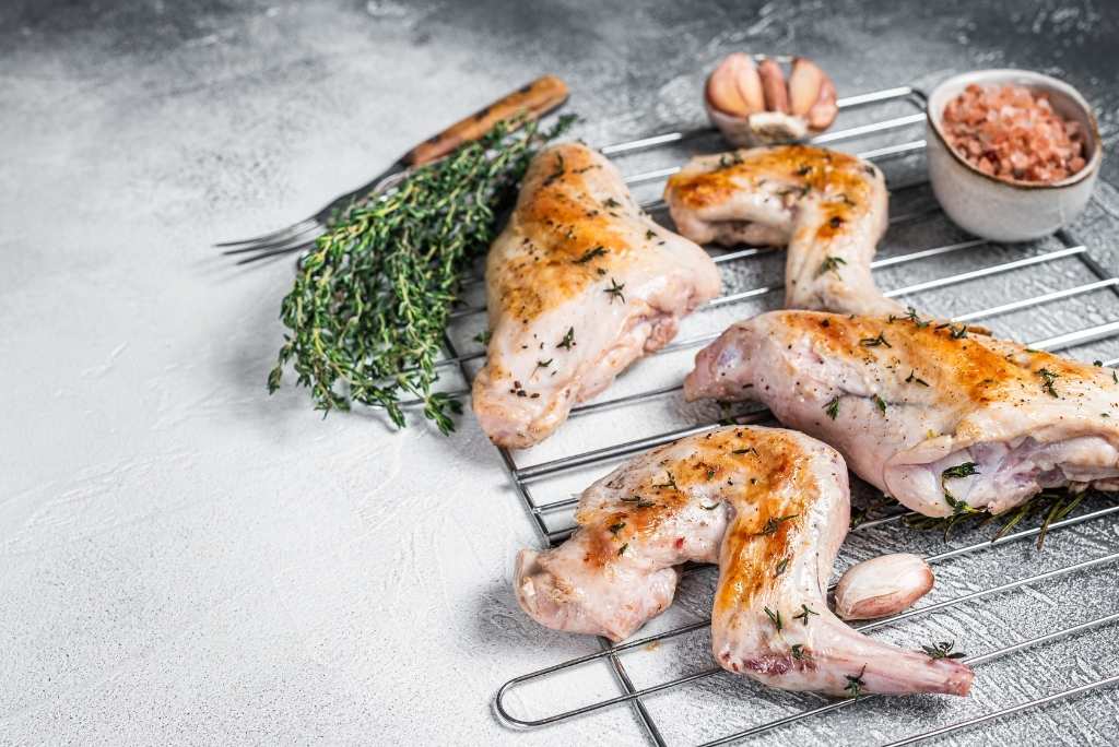 فيتامين B12 (الكوبالامين) قطع من لحم الأرنب المشوي على شبكة تبريد مع فصوص ثوم وأوراق زعتر.