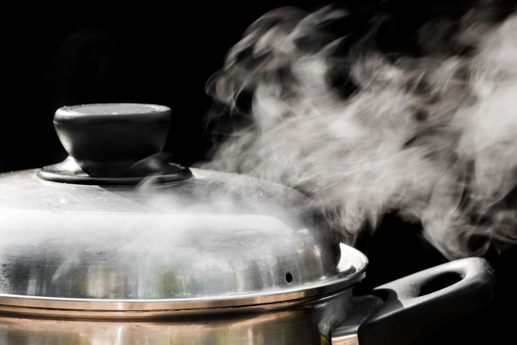 سحابة كبيرة من البخار تتصاعد من غطاء قدر معدني على خلفية داكنة.