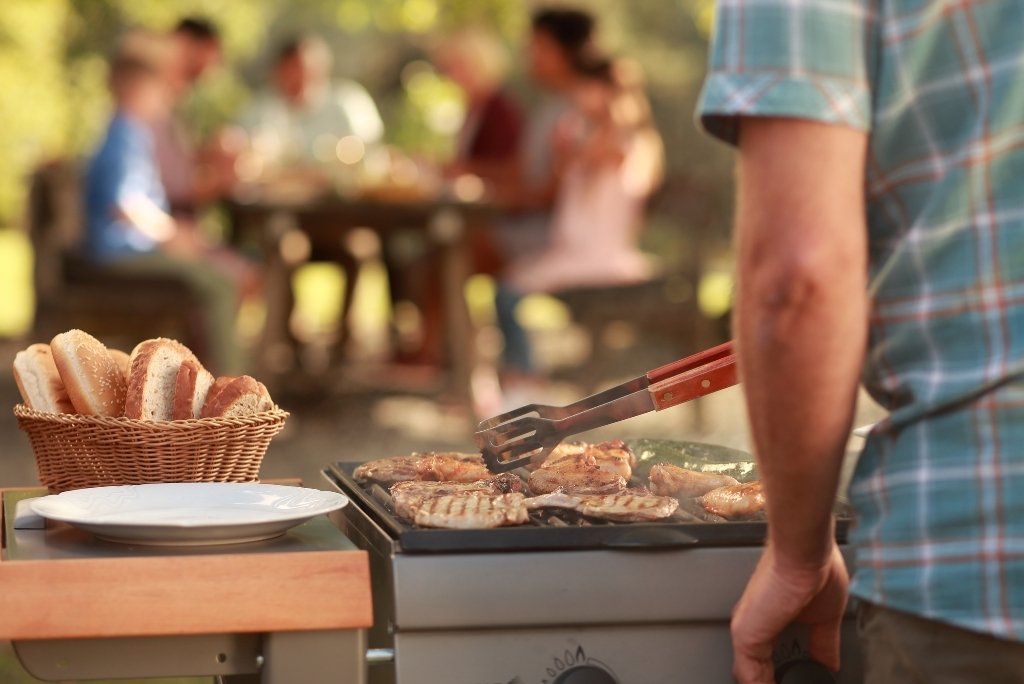 الطهي على الشواية رجل يحضر شواء في الهواء الطلق مع أصدقاء أو عائلة يجلسون في الخلفية.