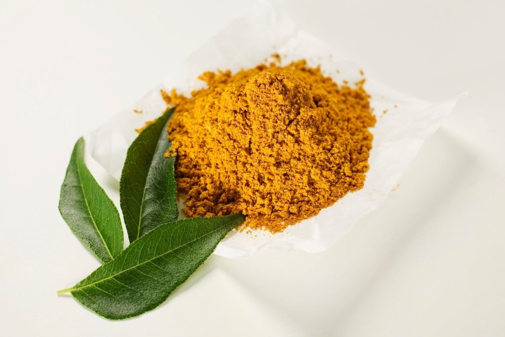 فوائد الكاري الصحية مسحوق كاري موضوع على ورقة بيضاء وبجانبه أوراق كاري خضراء.