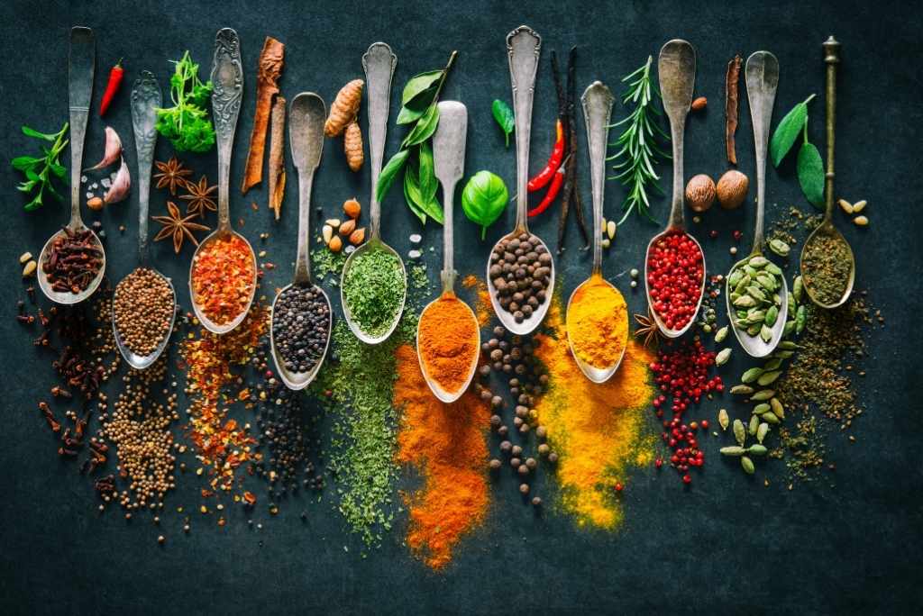 لماذا تستخدمون التوابل مع اللحوم؟ مجموعة من الملاعق تحتوي على أنواع مختلفة من التوابل والأعشاب، على خلفية داكنة.