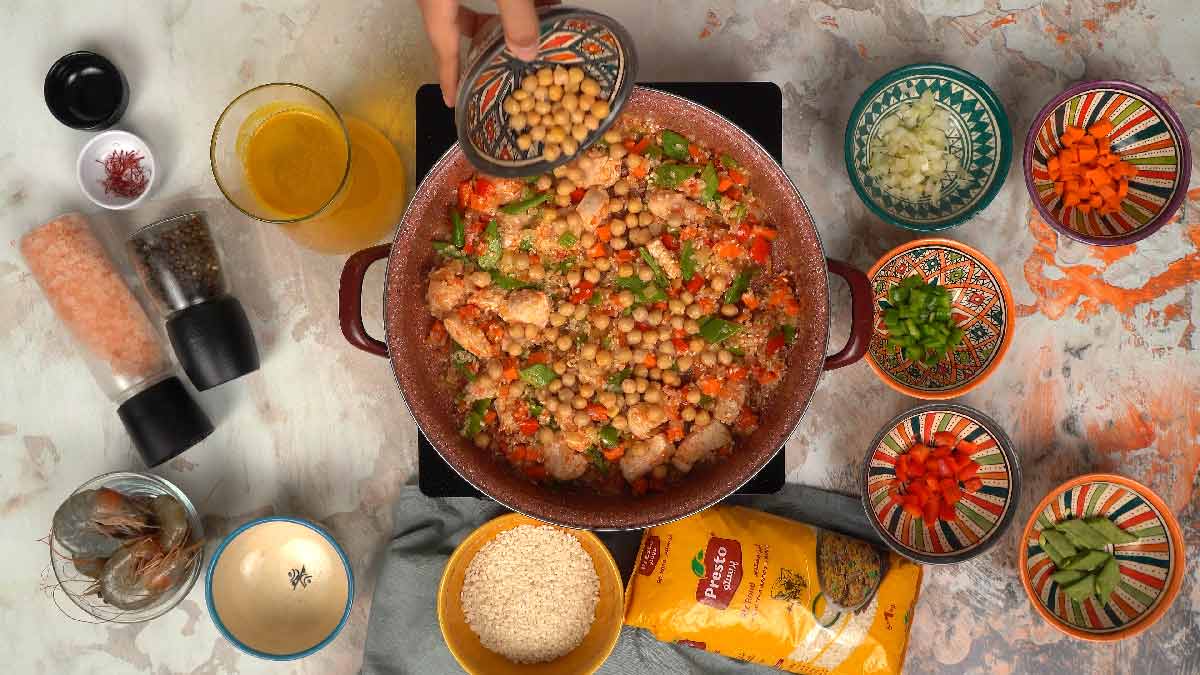 Une personne verse un bol de pois chiches cuits dans la poêle.
