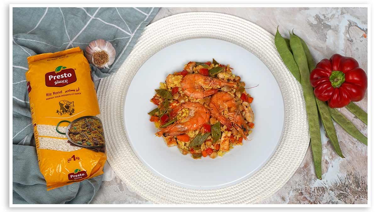 La paella aux pois chiches, avec des crevettes et des légumes, est servie dans une assiette blanche.