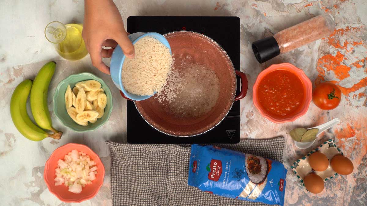 شخص يسكب أرز بريستو الطويل من وعاء في قدر على الموقد.
