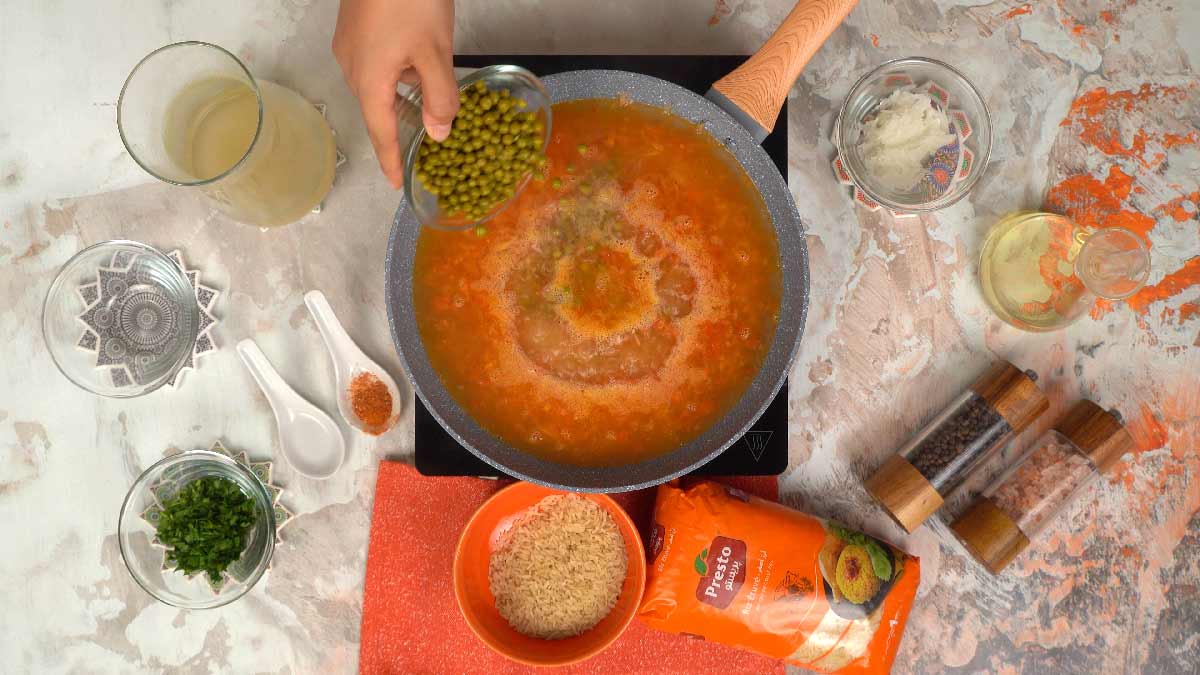شخص يضيف وعاء من البازلاء والمرق إلى المقلاة لطهي الأرز.
