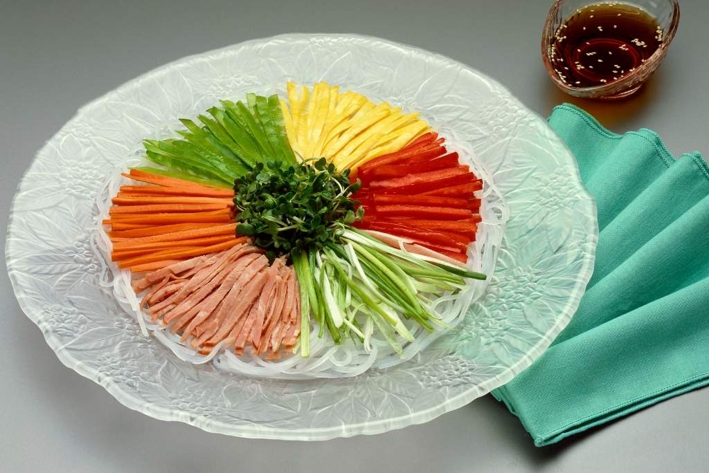 Un plat de nouilles et de légumes coupés en julienne disposés en cercle de différentes couleurs.