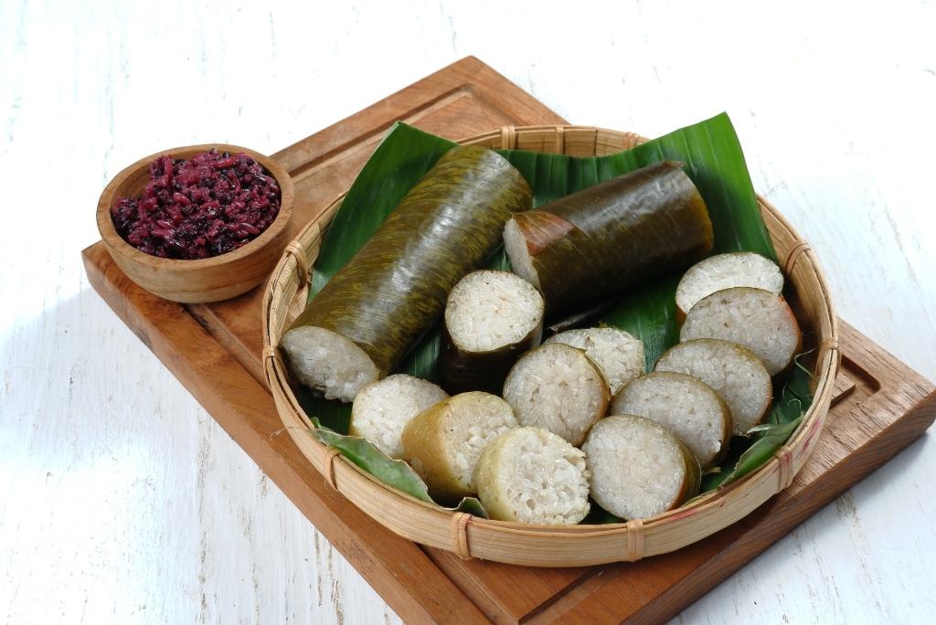 أرز لزج مطهو داخل أنابيب خيزران ومقطع إلى شرائح مرتبة في سلة خيزران مع طبق صغير من الصلصة بجانبه.