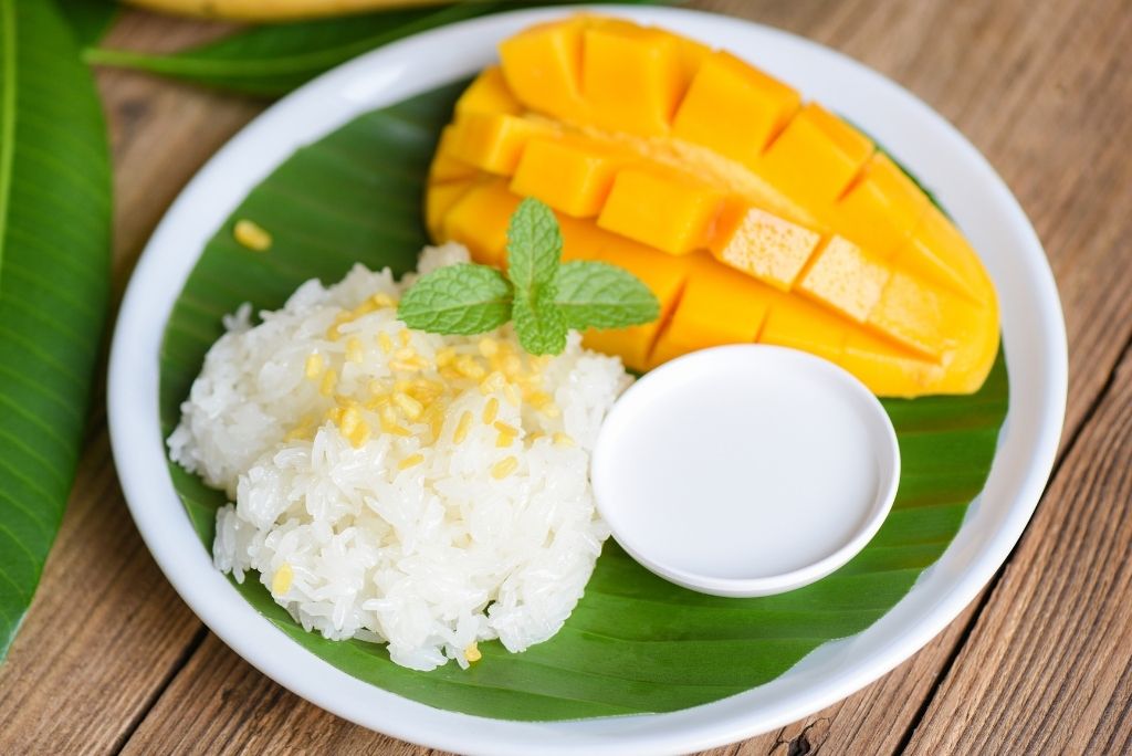 طبق حلوى الأرز اللزج مع شرائح المانجو وصلصة حليب جوز الهند وأوراق النعناع للتزيين.