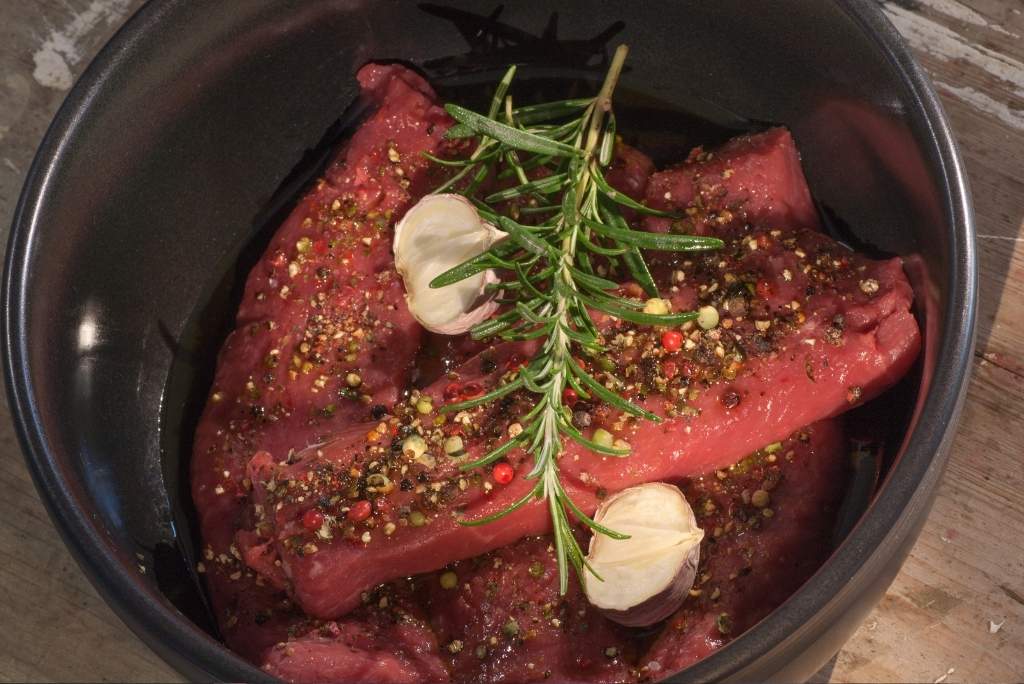 التوابل الثانوية للحوم لقطة مقربة للحوم نيئة متبلة بالأعشاب والثوم في وعاء داكن.