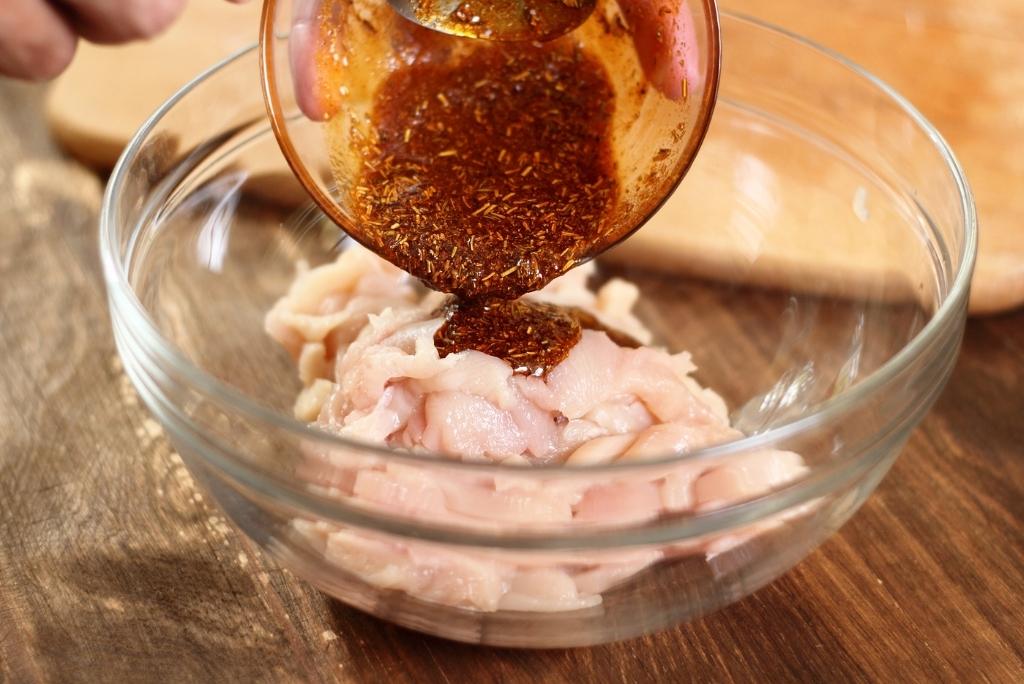 تحضير خلطات التوابل الخاصة بكم يدان تصبان تتبيلة على قطع دجاج نيئة في وعاء زجاجي.
