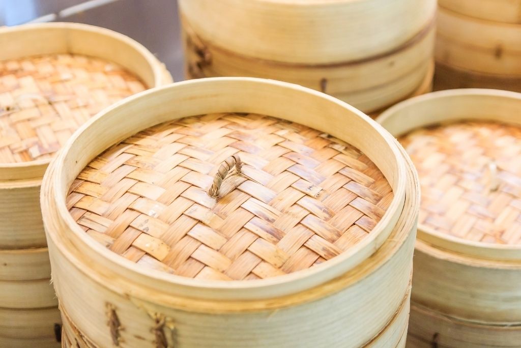 صورة مقربة لسلال الطهي بالبخار المصنوعة من الخيزران مكدسة فوق بعضها مع غطاء منسوج.